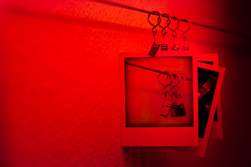 Fotos hängen bei Rotlicht zum Trocknen mit Klammern fixiert an einer Leine in der Dunkelkammer.